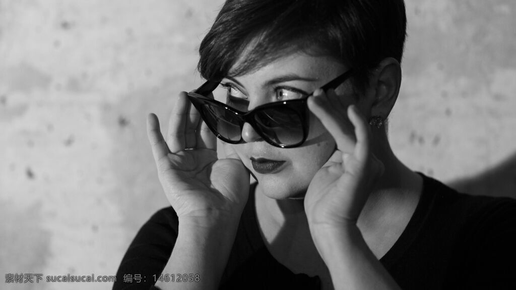 黑白摄影 短发女性 墨镜 时尚风格 个性造型 手扶墨镜 简约背景 酷炫形象 黑色上衣 饰品耳环 高冷气质 女性魅力 优雅姿态